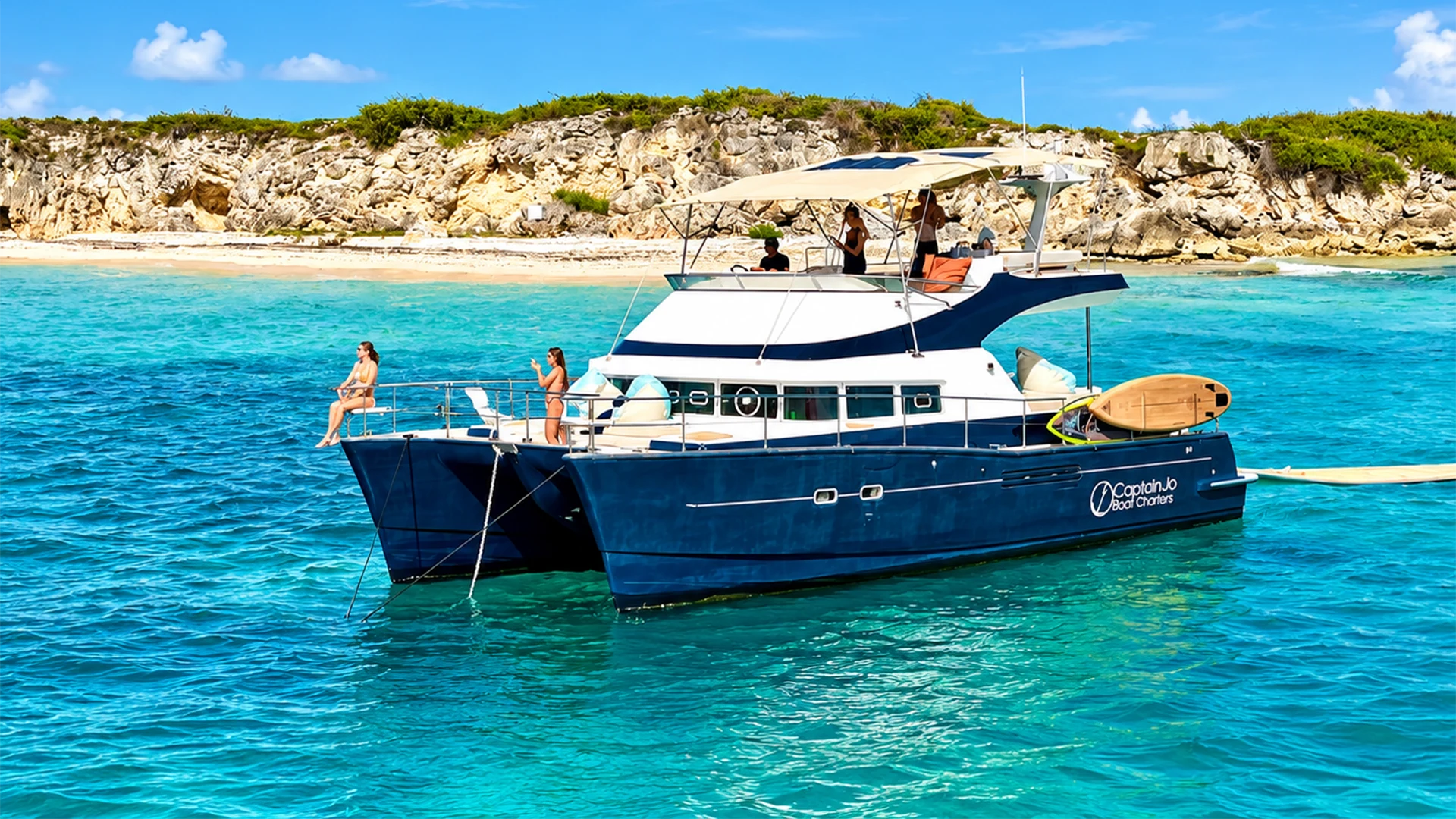 Seaview Powercat 44 with navy-blue twin hulls, shaded flybridge, and guests relaxing aboard near a rocky Caribbean beach
